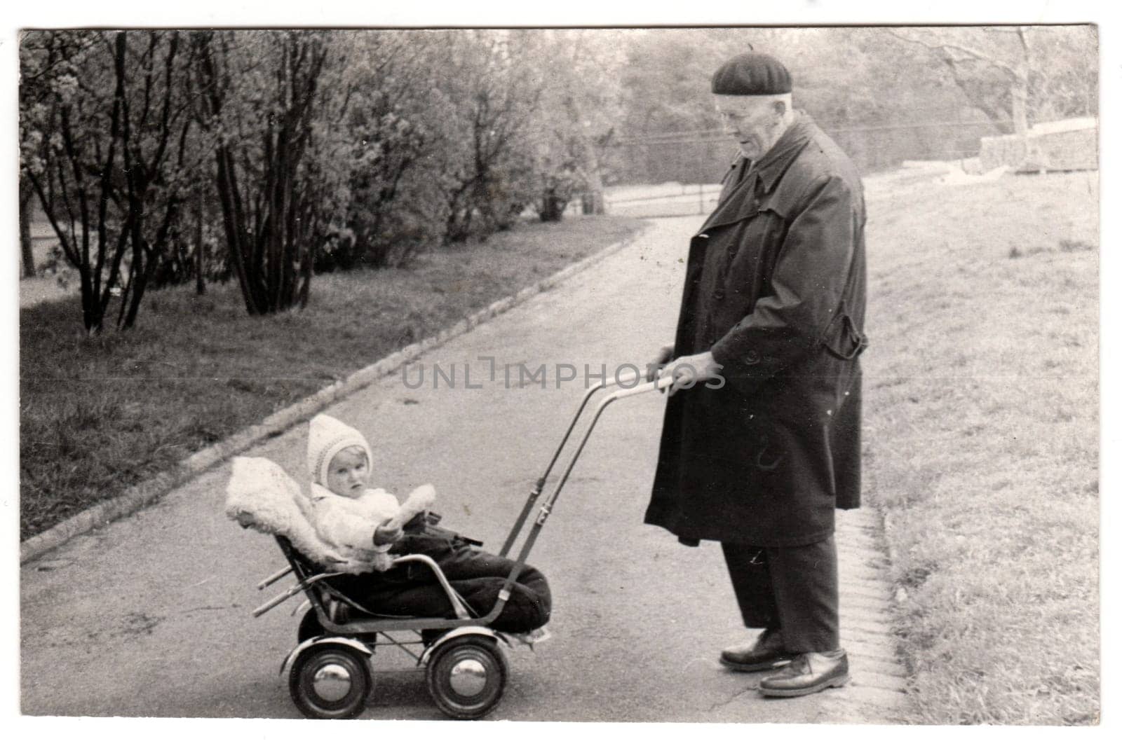 Vintage photo shows grandfather with a small baby in the pram - carriage. Retro black and white photography. Circa 1950. by roman_nerud