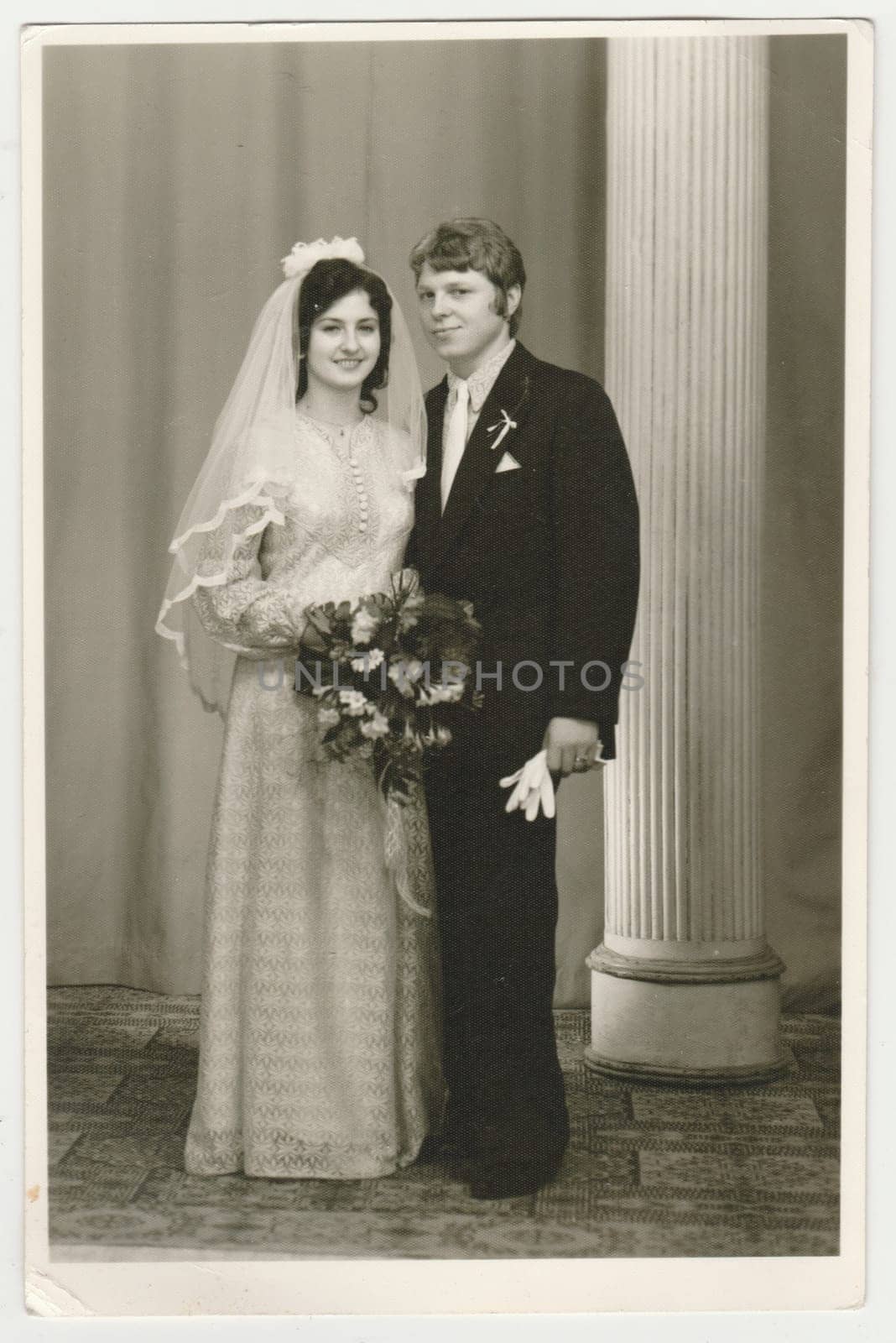 Vintage photo shows a bride with bridegroom. Bride wears a soft veil and holds wedding flowers - bouquet. Retro black and white photography. Circa 1980. by roman_nerud