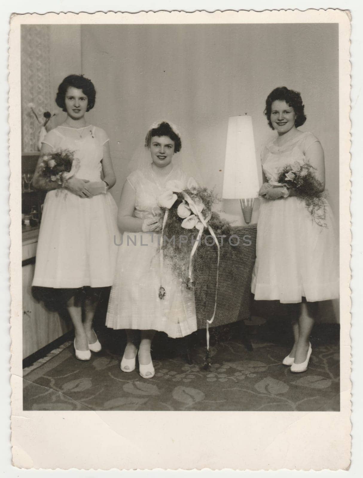 Vintage photo shows a bride with bridesmaids. Bride wears a soft veil and holds calla flowers - bouquet. Retro black and white photography. Circa 1960. by roman_nerud