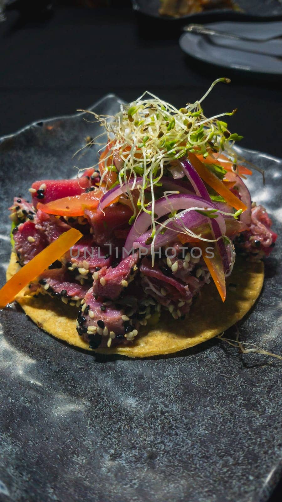 Tostada with raw tuna fish ceviche and fresh vegetables. Mexican gourmet seafood on dark background.