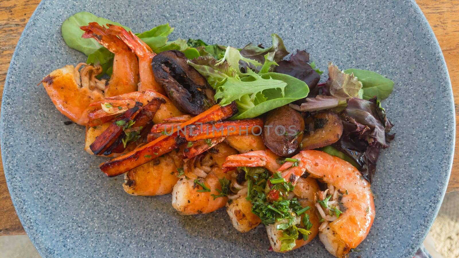 Shrimp with garlic butter and chimichurri sauce, camarones al ajo, delicious Mexican seafood dish with salad leaves on grey stone plate.