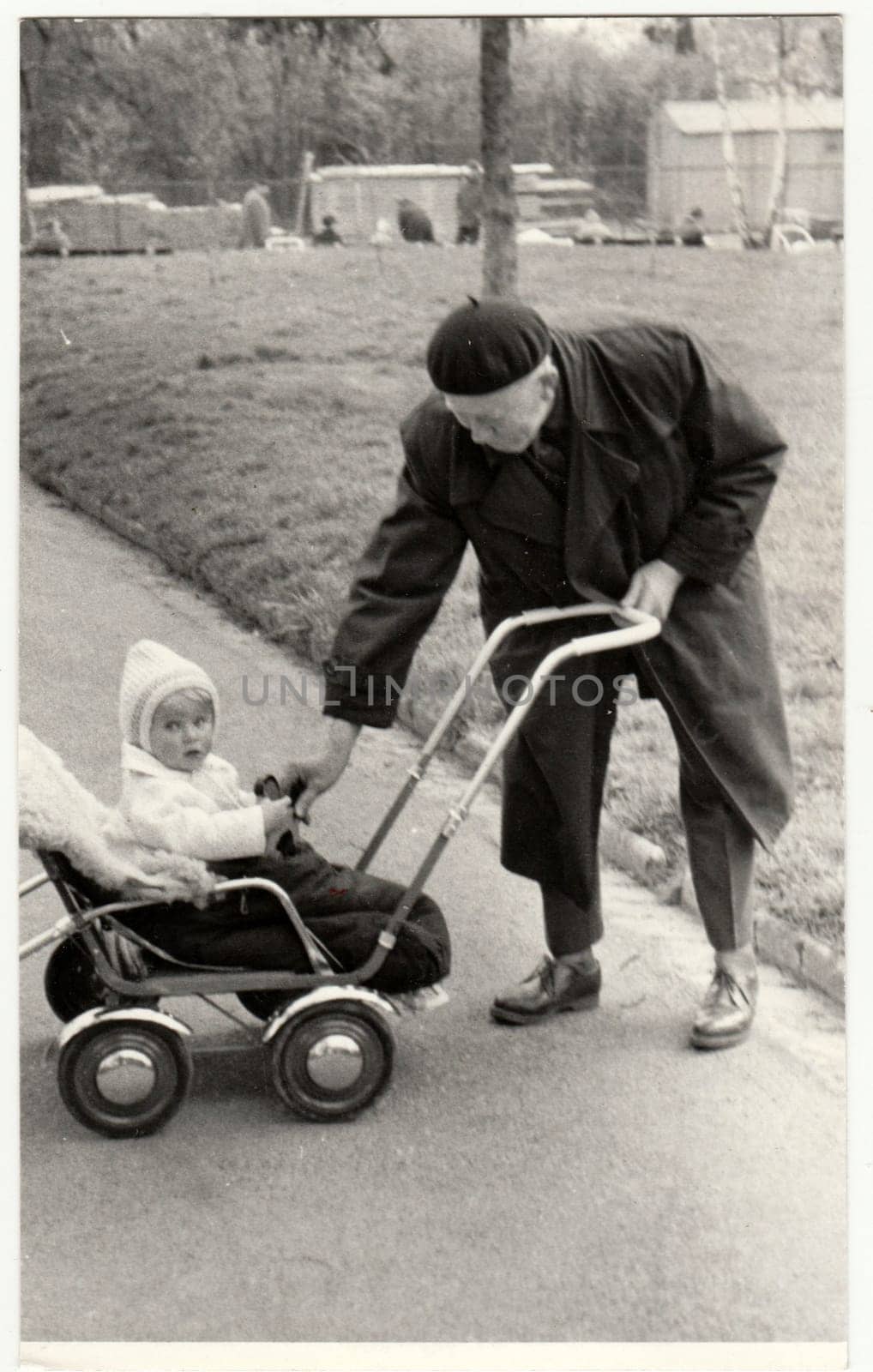 Vintage photo shows grandfather with a small baby in the pram - carriage. Retro black and white photography. Circa 1950. by roman_nerud