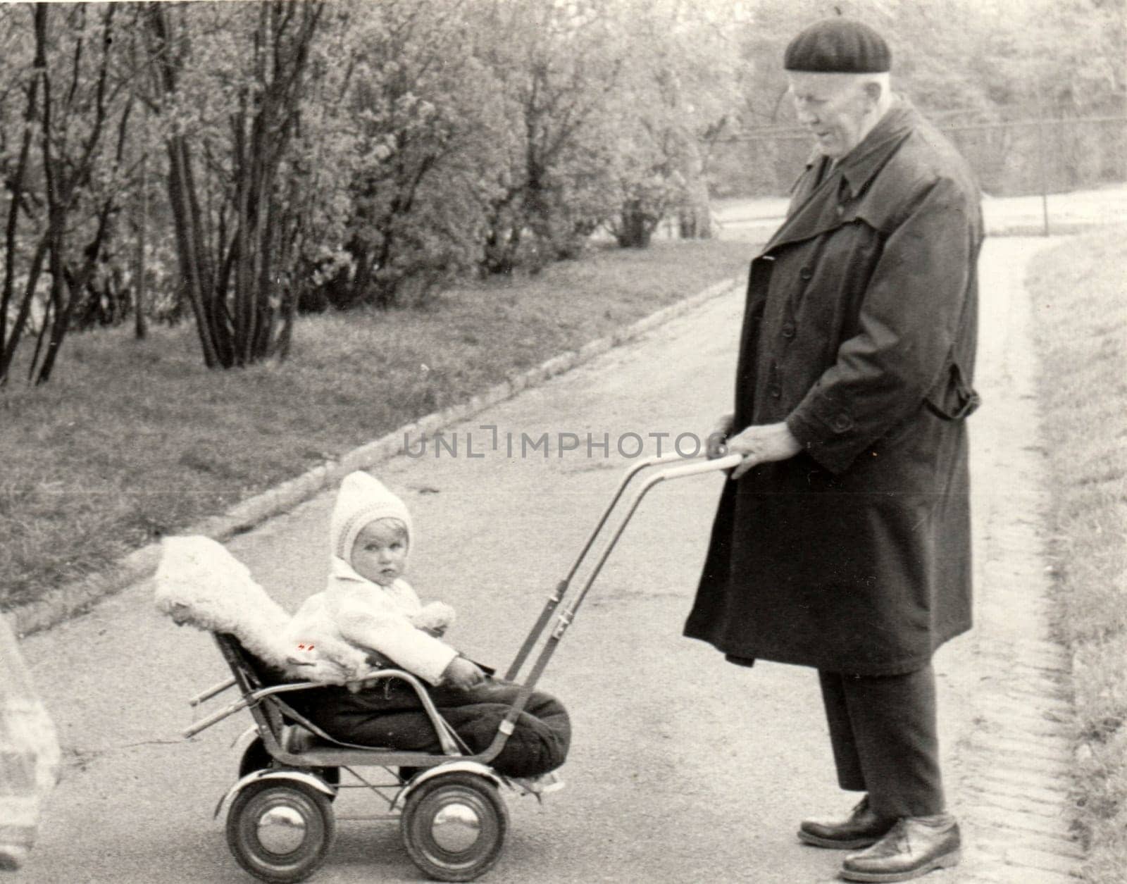 Vintage photo shows grandfather with a small baby in the pram - carriage. Retro black and white photography. Circa 1950. by roman_nerud