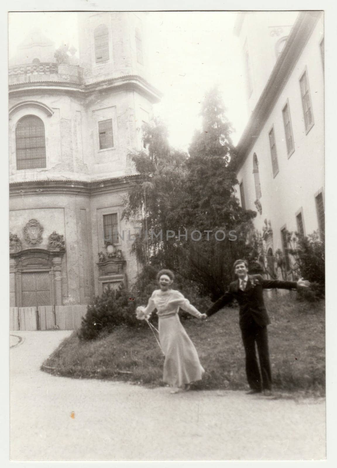 Vintage photo shows young newlyweds - bridal couple in front of church. Retro black and white photography. Circa 1980. by roman_nerud