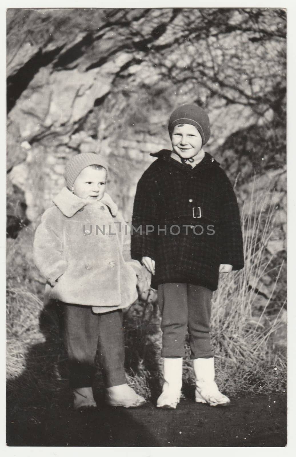 Vintage photo shows small children stand outdoors in the wintertime. Retro black and white photography. Circa 1950. by roman_nerud