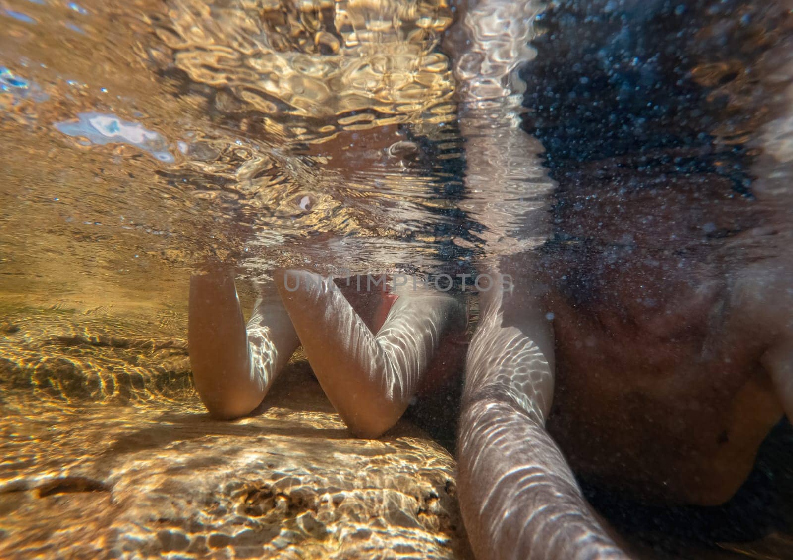 A male and female body under the water, unrecognizable, lying in a shallow river area, enjoying the moment, the anonymity, with space for text and lots of water.