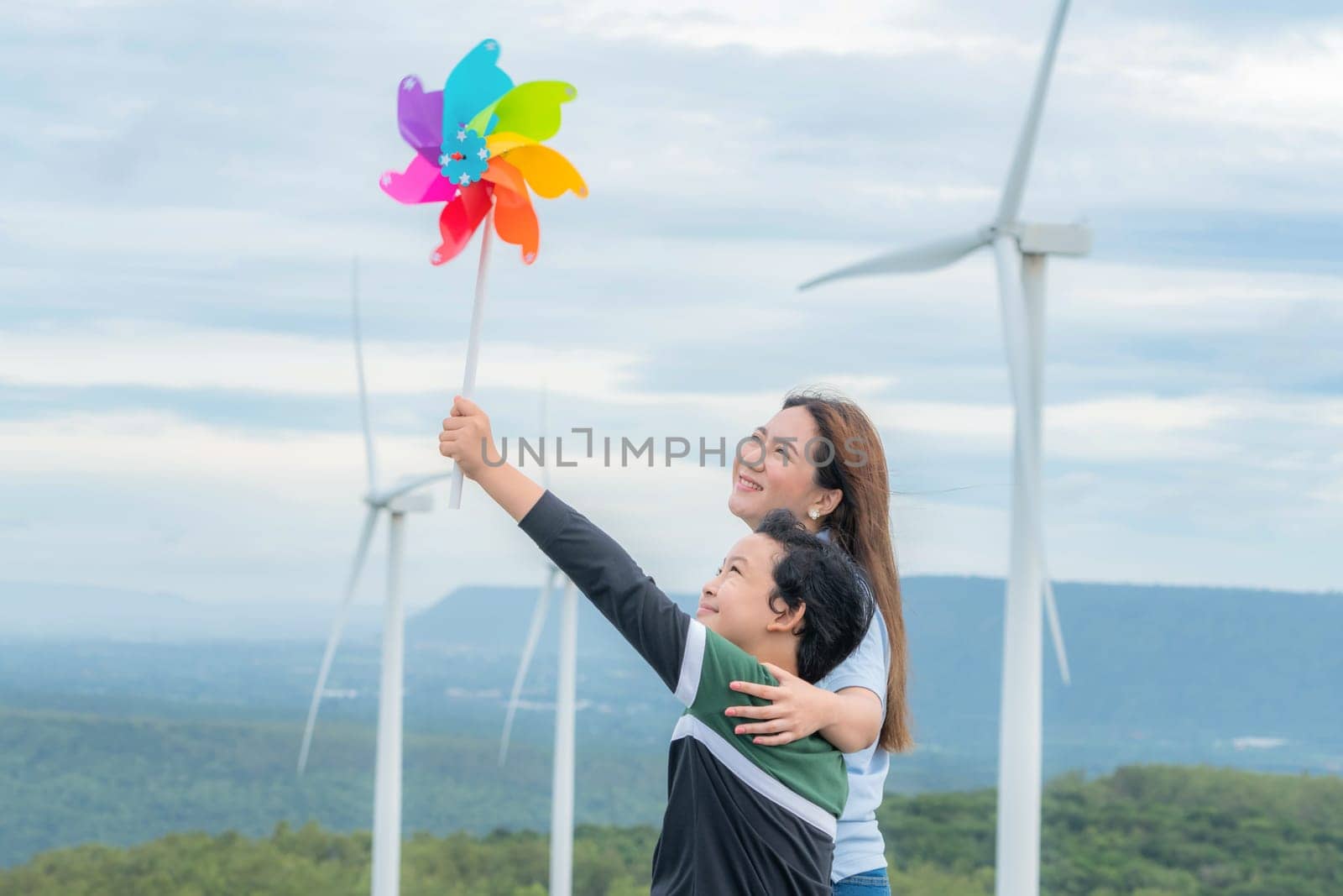 A progressive mother and her son are on vacation, enjoying the natural beauty of a lake at the bottom of a hill while the boy carries a toy windmill.