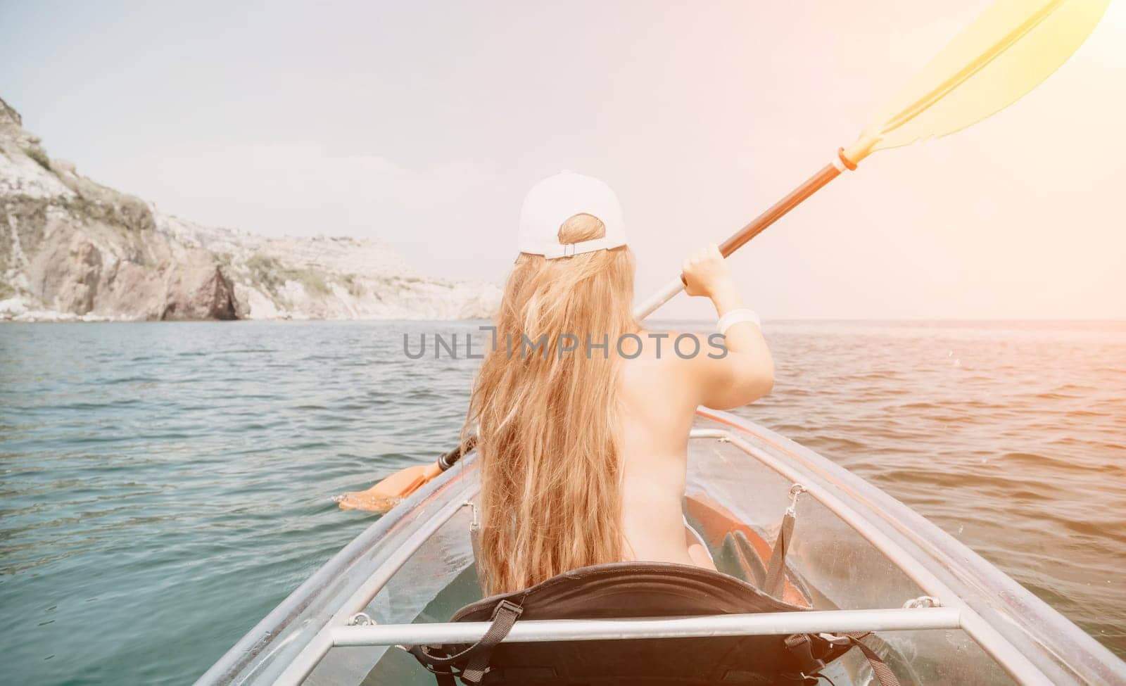 Woman in kayak back view. Happy young woman with long hair floating in transparent kayak on the crystal clear sea. Summer holiday vacation and cheerful female people having fun on the boat.