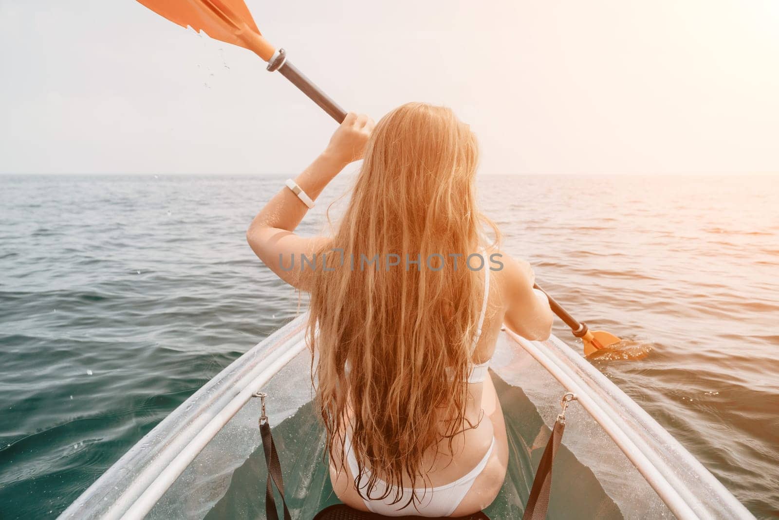 Woman in kayak back view. Happy young woman with long hair floating in transparent kayak on the crystal clear sea. Summer holiday vacation and cheerful female people having fun on the boat.