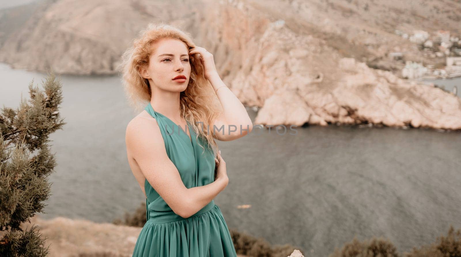 Redhead woman portrait. Curly redhead young caucasian woman with freckles looking at camera and smiling. Close up portrait cute woman in a mint long dress posing on a volcanic rock high above the sea by panophotograph