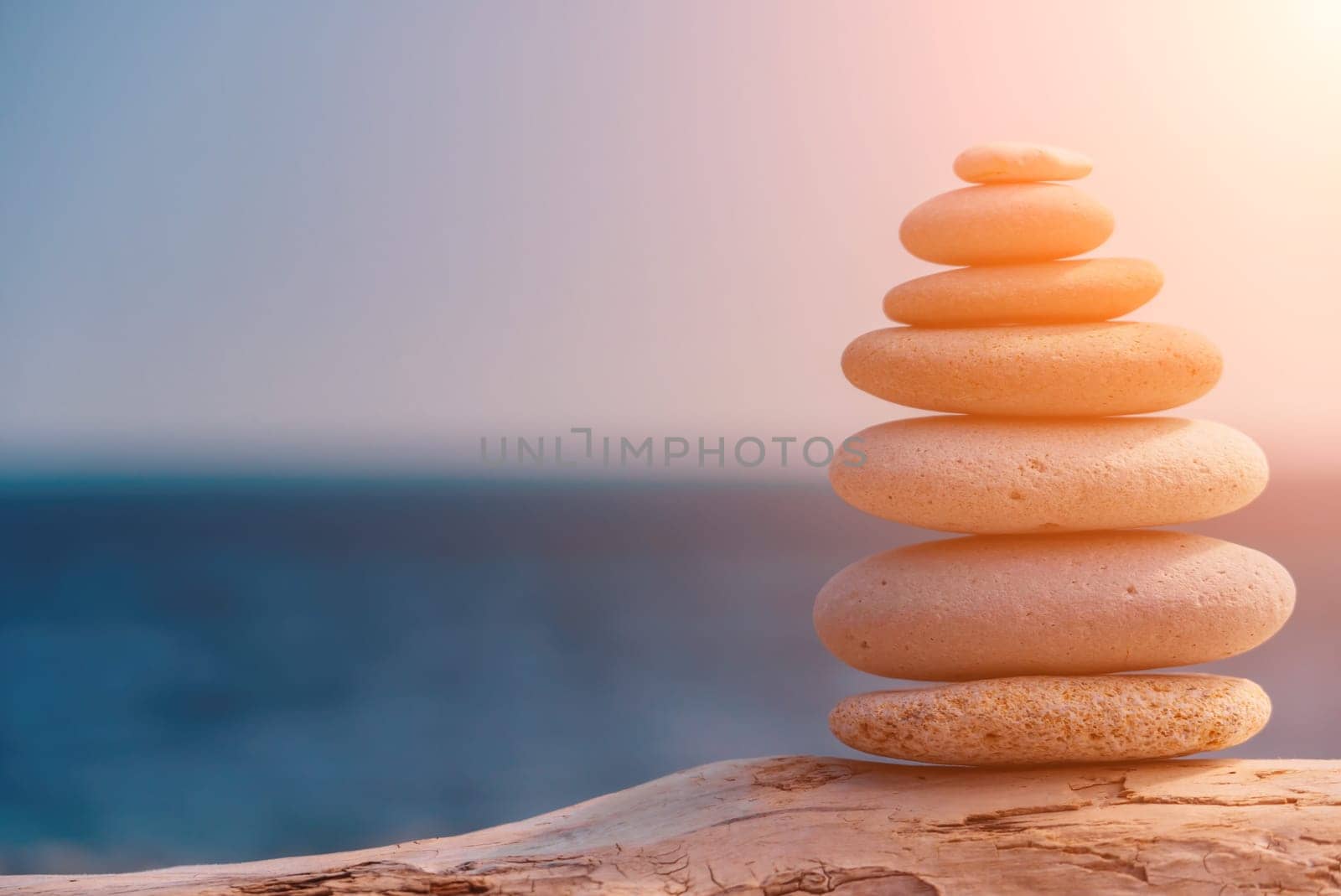 Balanced rock pyramid on sea pebbles beach, sunny day and clear sky at sunset. Golden sea bokeh on background. Selective focus, zen stones on sea beach, meditation, spa, harmony, calm, balance concept by panophotograph