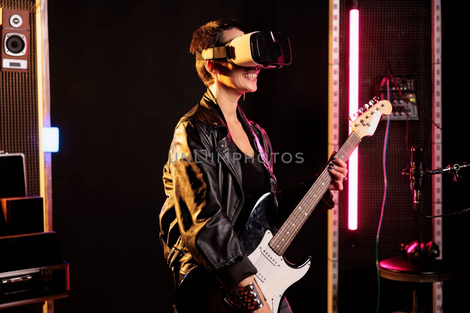 Rebel rockstar playing heavy metal song using electric guitar while wearing vr goggles to have rock concert simultation, enjoying experience in music studio. Woman musician working at new grunge album