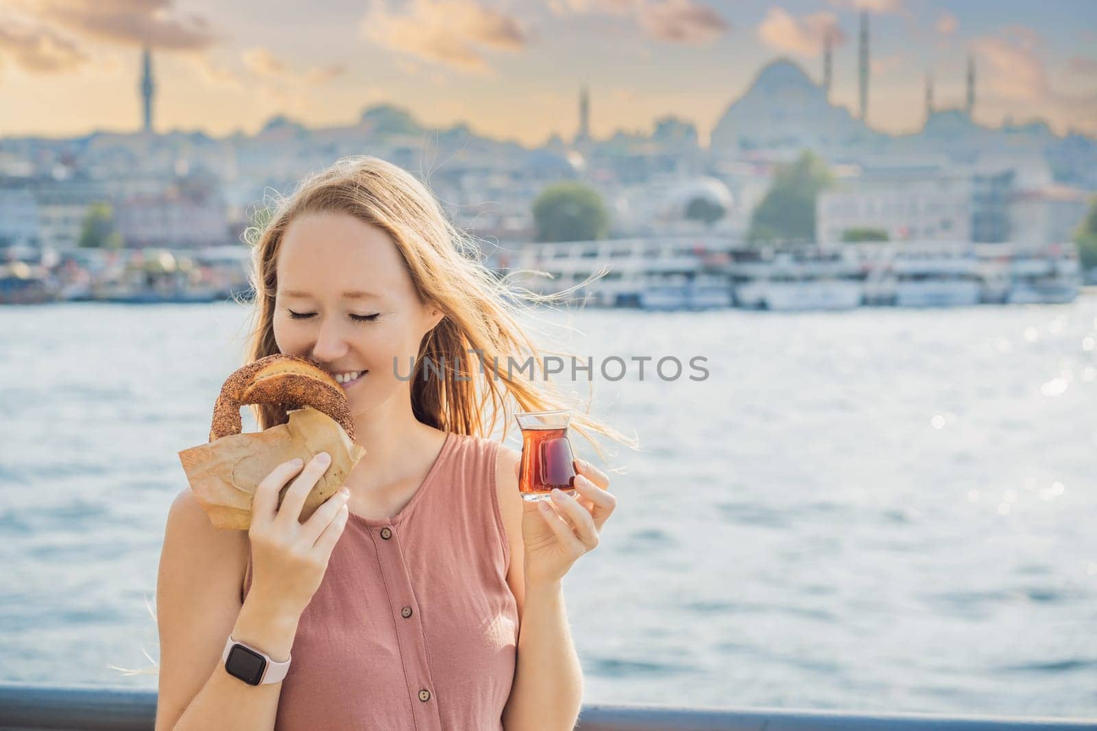 Woman in Istanbul having breakfast with Simit and a glass of Turkish tea. Glass of Turkish tea and bagel Simit against golden horn bay in Istanbul, Turkey. Turkiye.