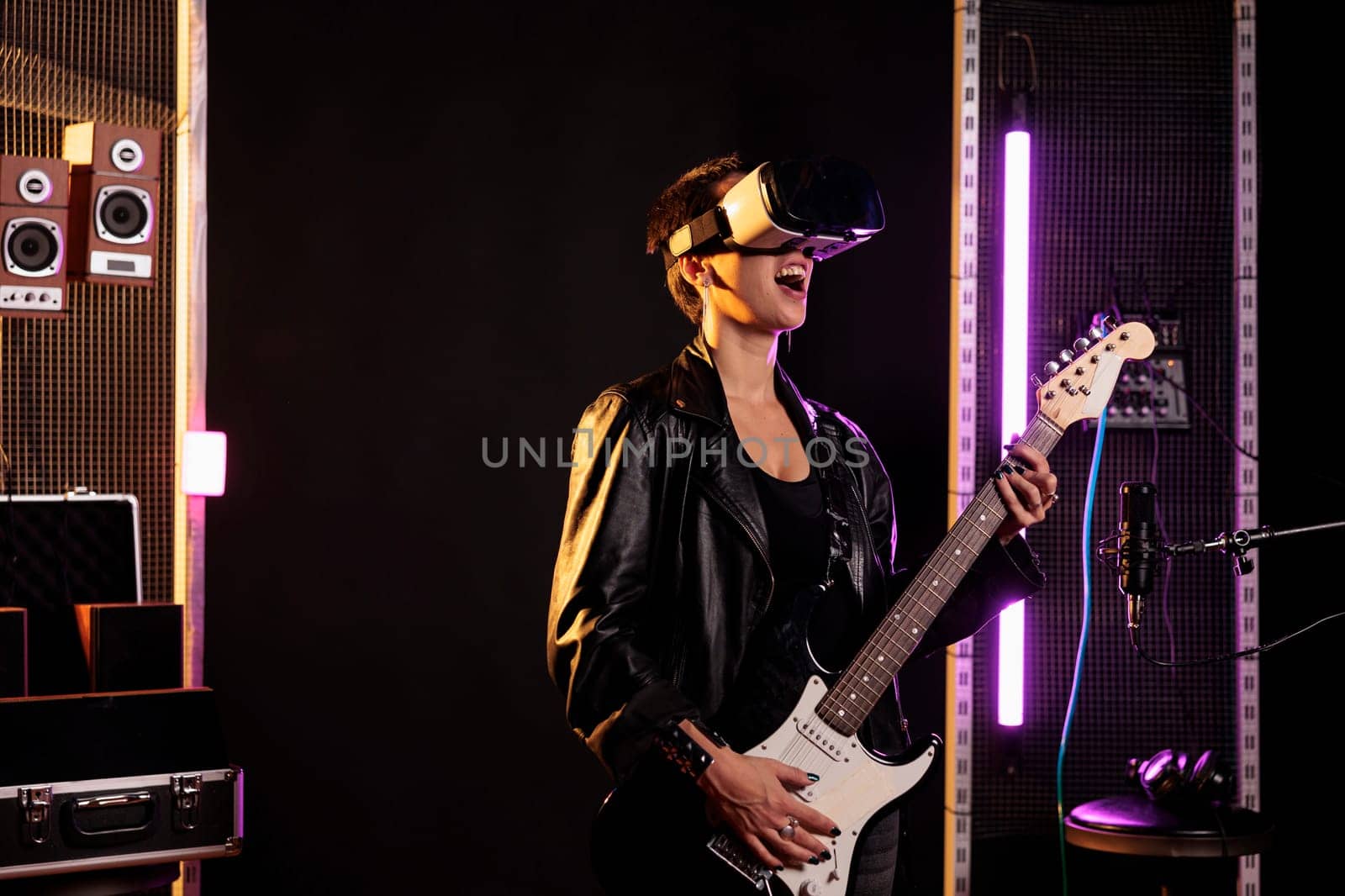 Rockstar with vr goggles enjoying rock concert simulation while playing heavy metal song at electric guitar in music studio. Woman musician performing grunge album using electricinstrument