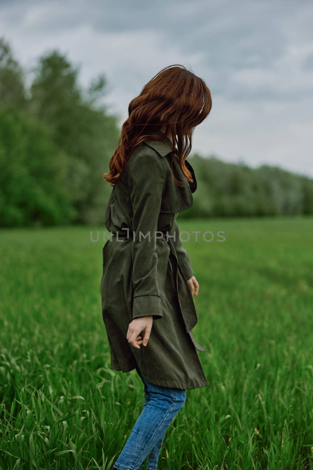 a woman with long red hair stands with her back to the camera in a field in tall green grass by Vichizh