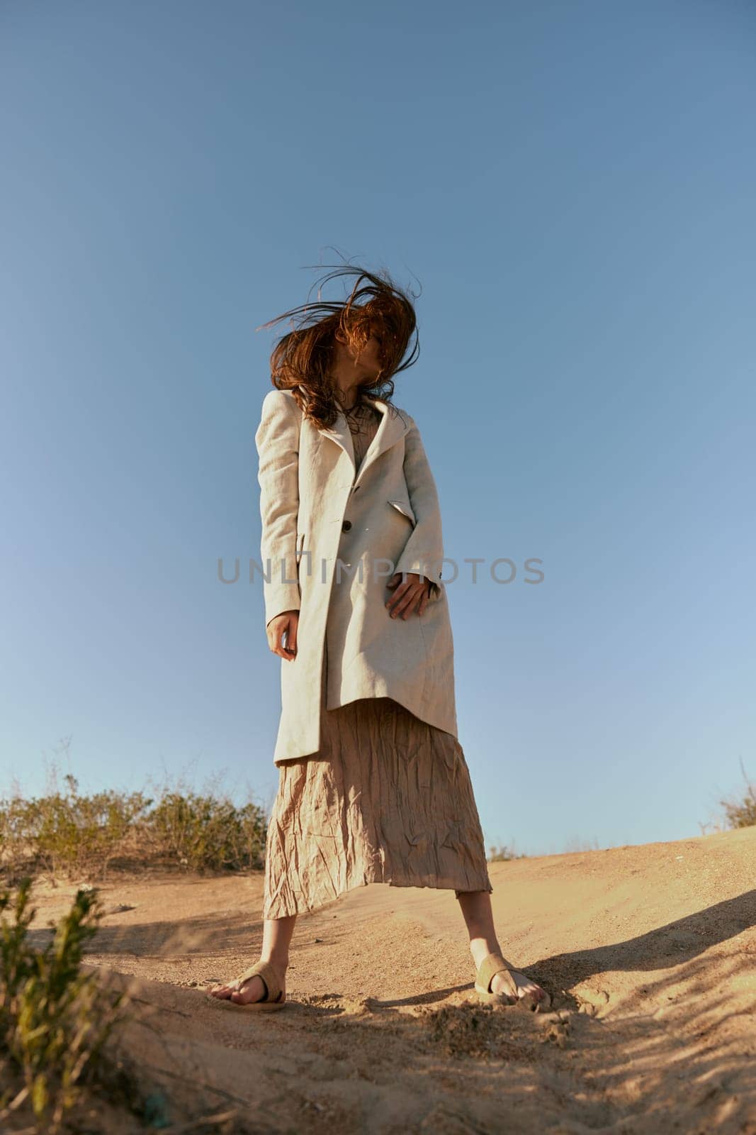 stylish woman in fashion style posing on the sand covering her face with her hair in motion. High quality photo