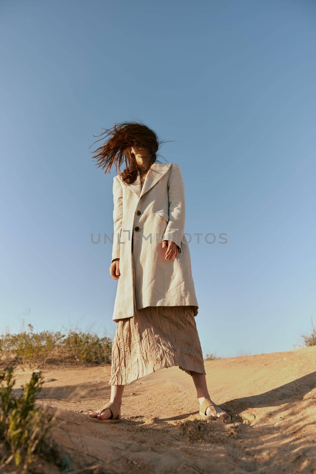 stylish woman in fashion style posing on the sand covering her face with her hair in motion. High quality photo