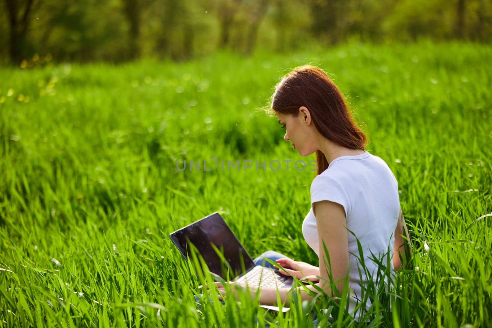 a woman with laptop sitting in a city park on the lawn on a hot summer day by Vichizh