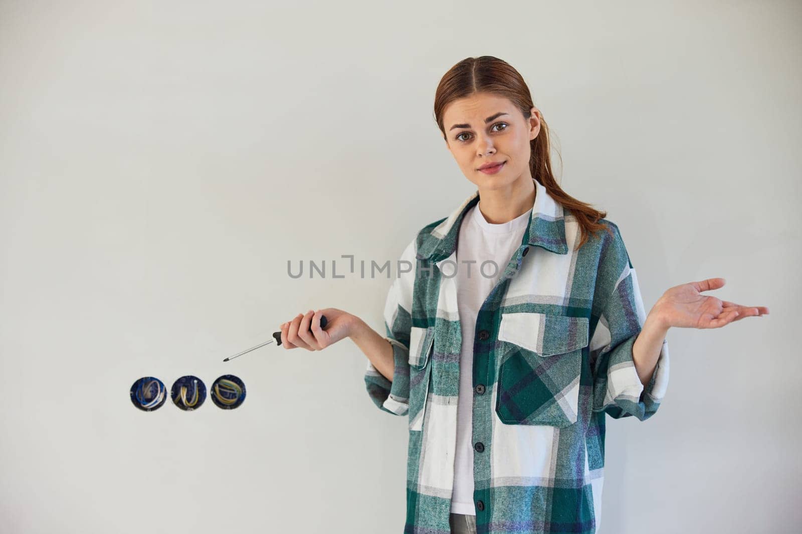 a woman making repairs at home spreads her hands in surprise while standing next to the sockets by Vichizh