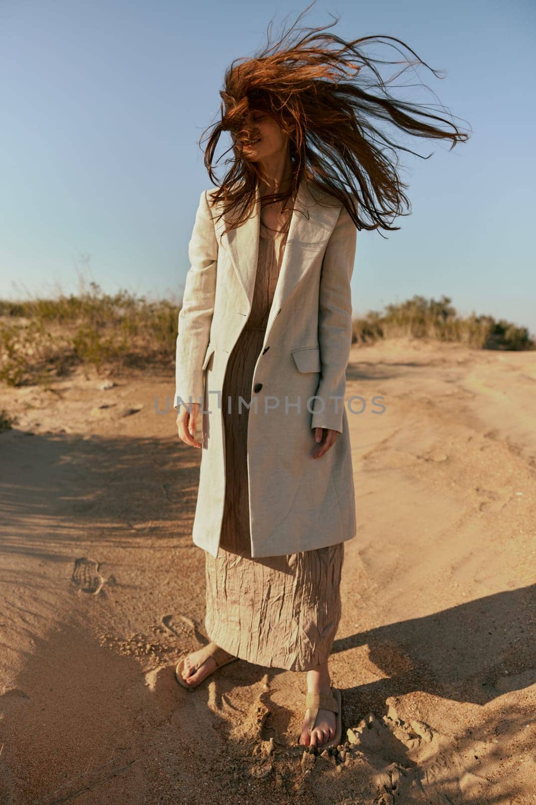 a woman with long red hair blown in the wind stands in stylish clothes on the sand. High quality photo
