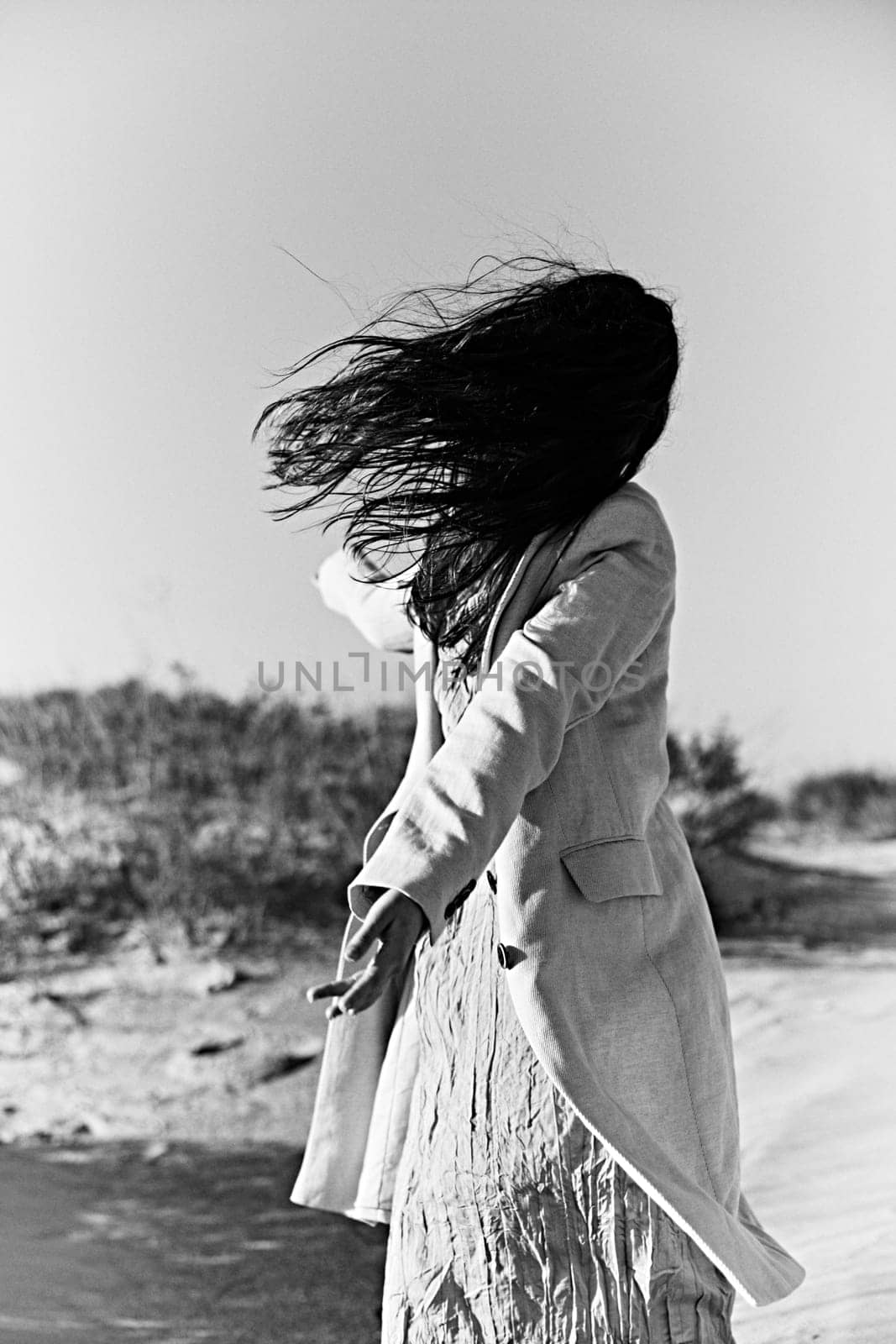 monochrome photo of a twirling woman on the coast in a light-colored jacket