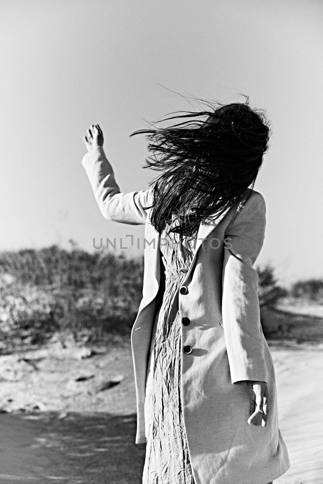 monochrome photo of a twirling woman on the coast in a light-colored jacket by Vichizh