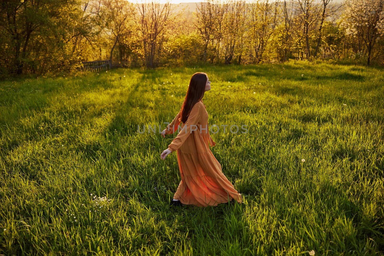 a joyful woman runs through a green field with her hands behind her back, enjoying a warm summer day and nature during the sunset. Horizontal photography in nature. High quality photo