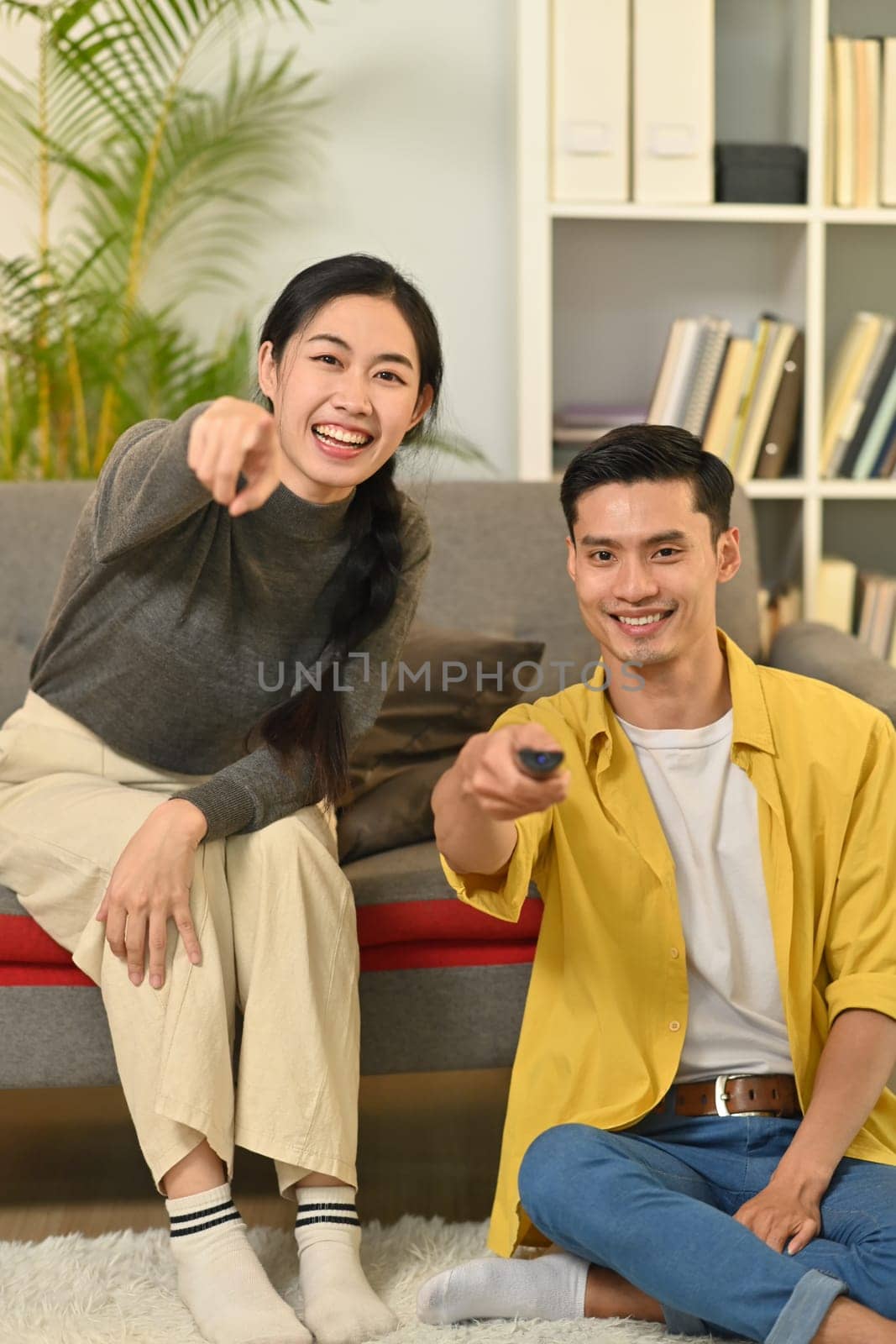 Joyful young couple relaxing and watching TV together on a couch in cozy home. People and leisure activity concept.