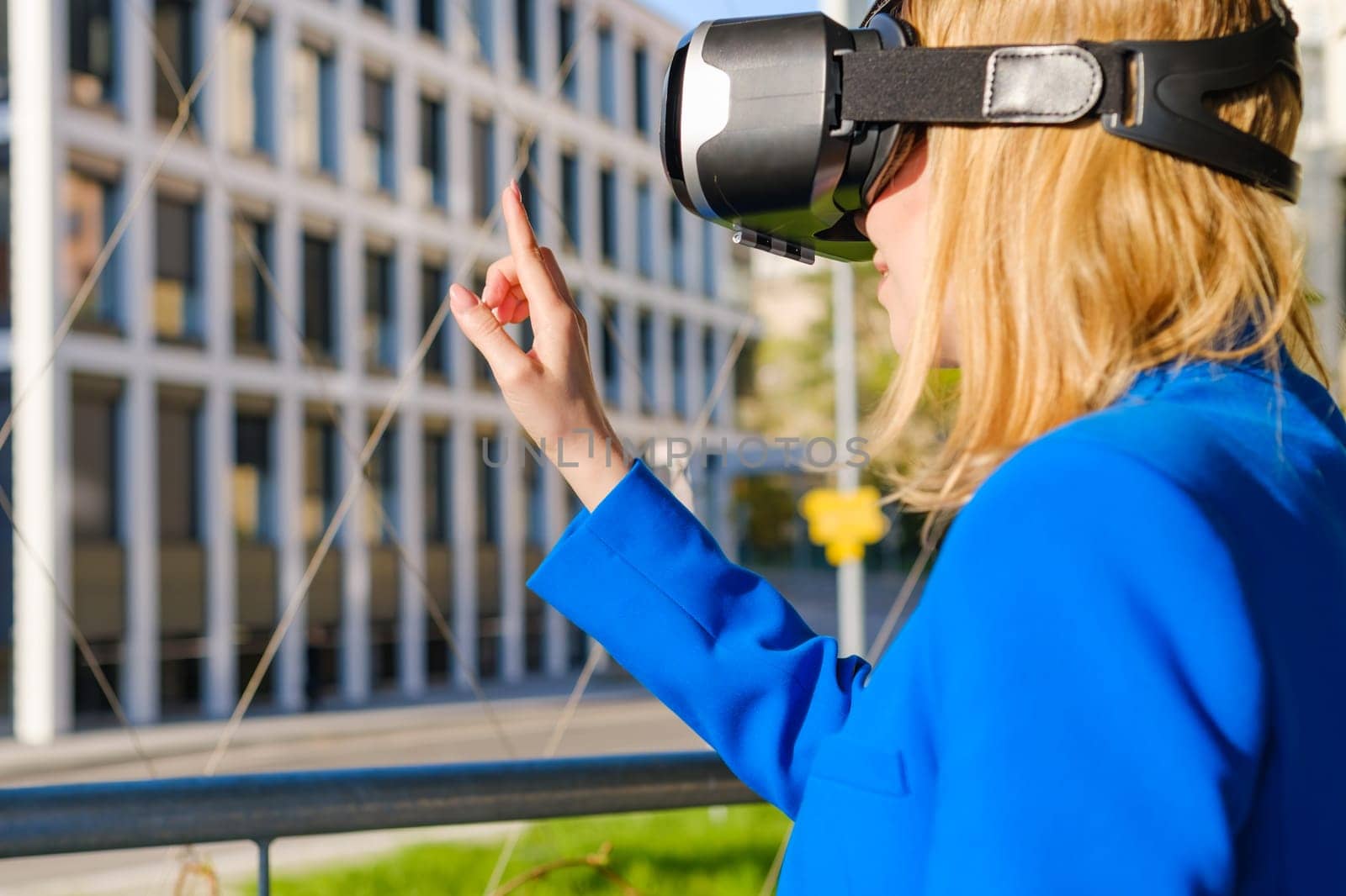 Young woman touching the air using a virtual interface by pressing buttons finger in virtual reality glasses near business center.