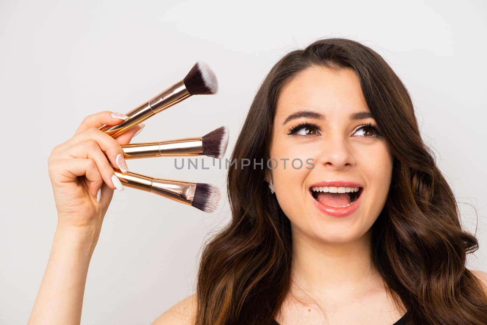 Positive attractive woman holding cosmetic makeup brushes over gray background.