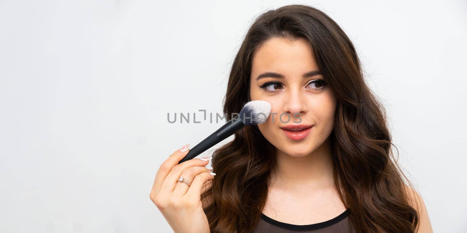 Beautiful makeup artist applies powder on cheek on the white background with copy space.
