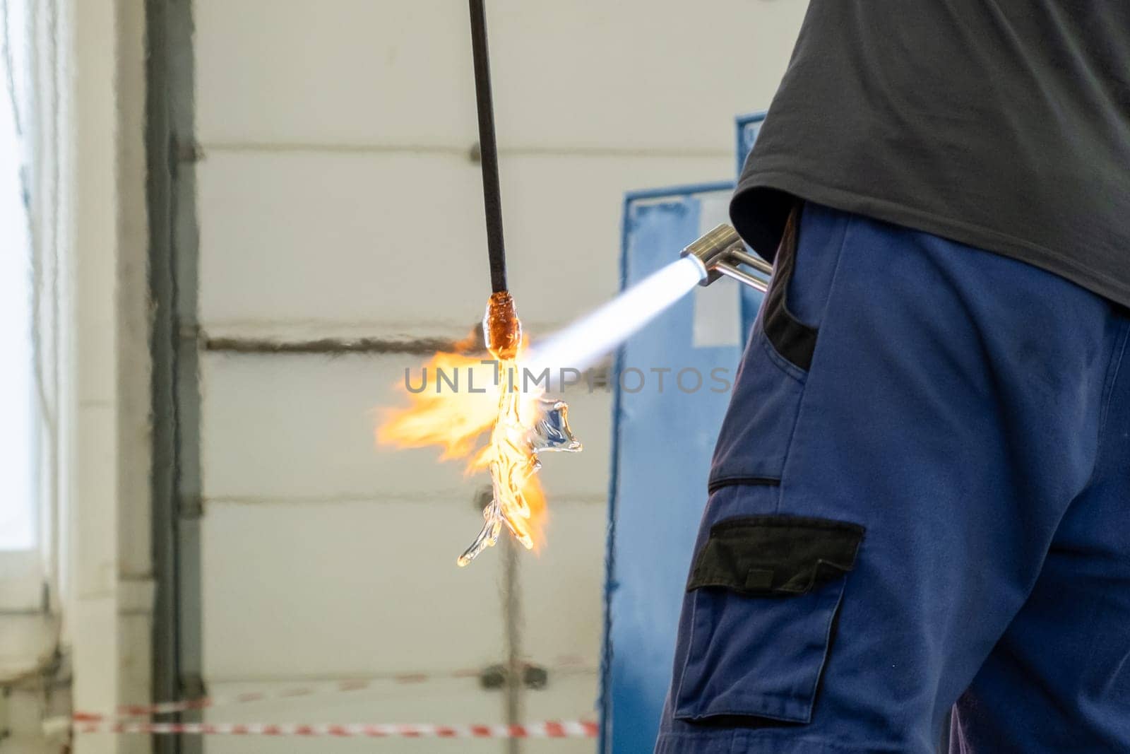 A man uses a gas burner to melt glass. A craftsman makes a glass in a leaf shaped.