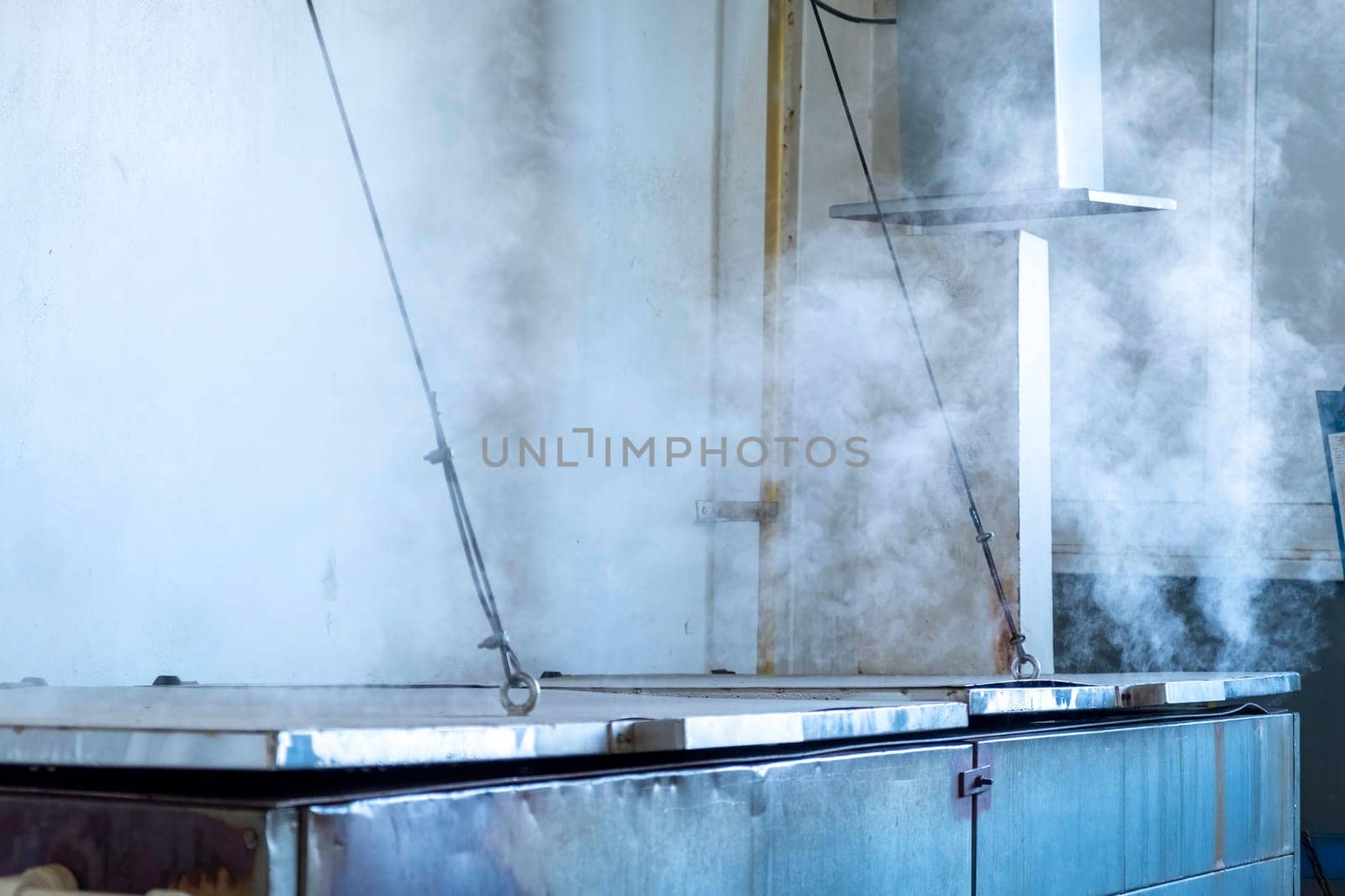 Large oven closed with metal lids and rising up hot steam cloud in spacious workshop of old traditional glassblowing plant