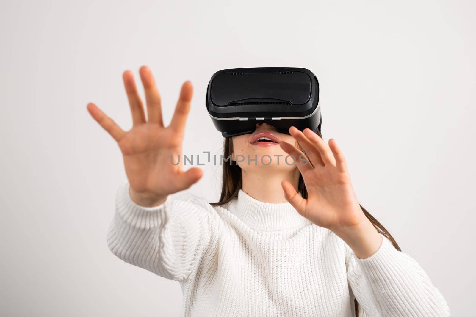 Woman enjoys virtual reality looking through VR goggles at home. Young female person experiences modern technology standing against window