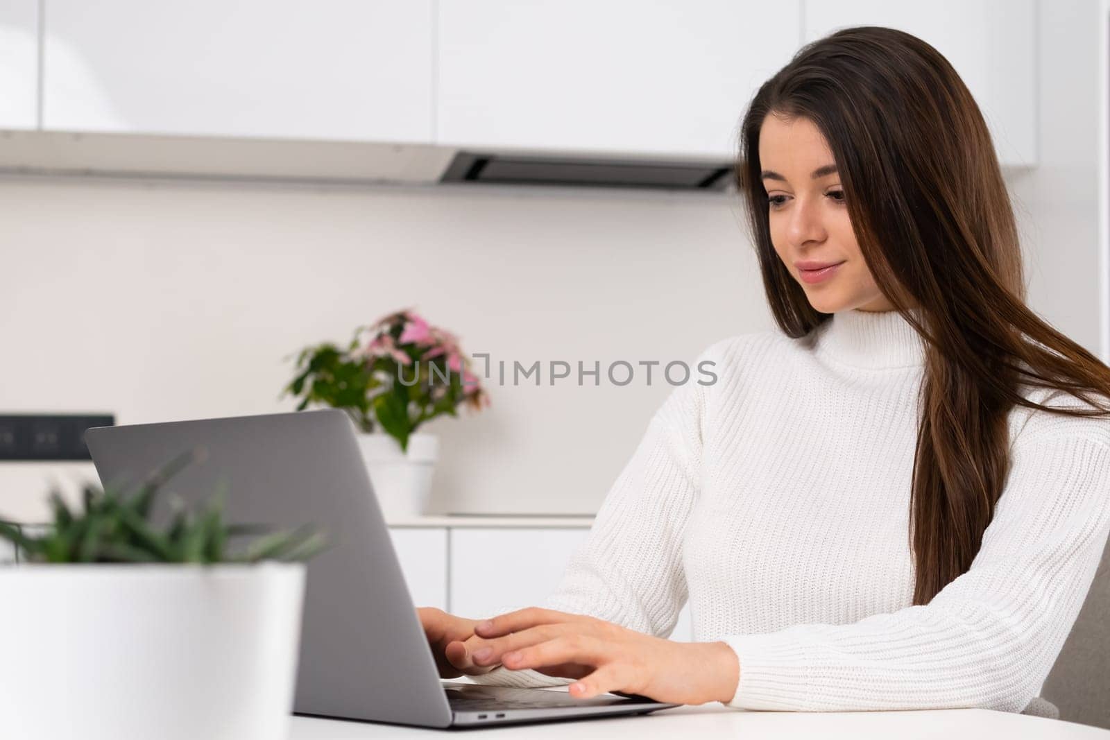Joyful business woman working at home using a laptop. Blogger or freelancer works on her startup at home in modern Scandinavian interior