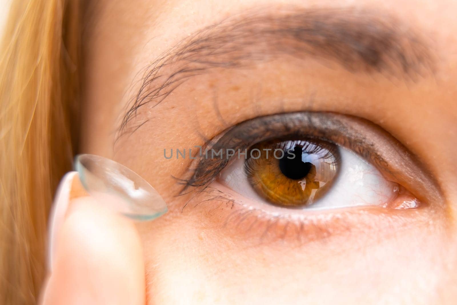 Young woman holding contact lens near her brown eye