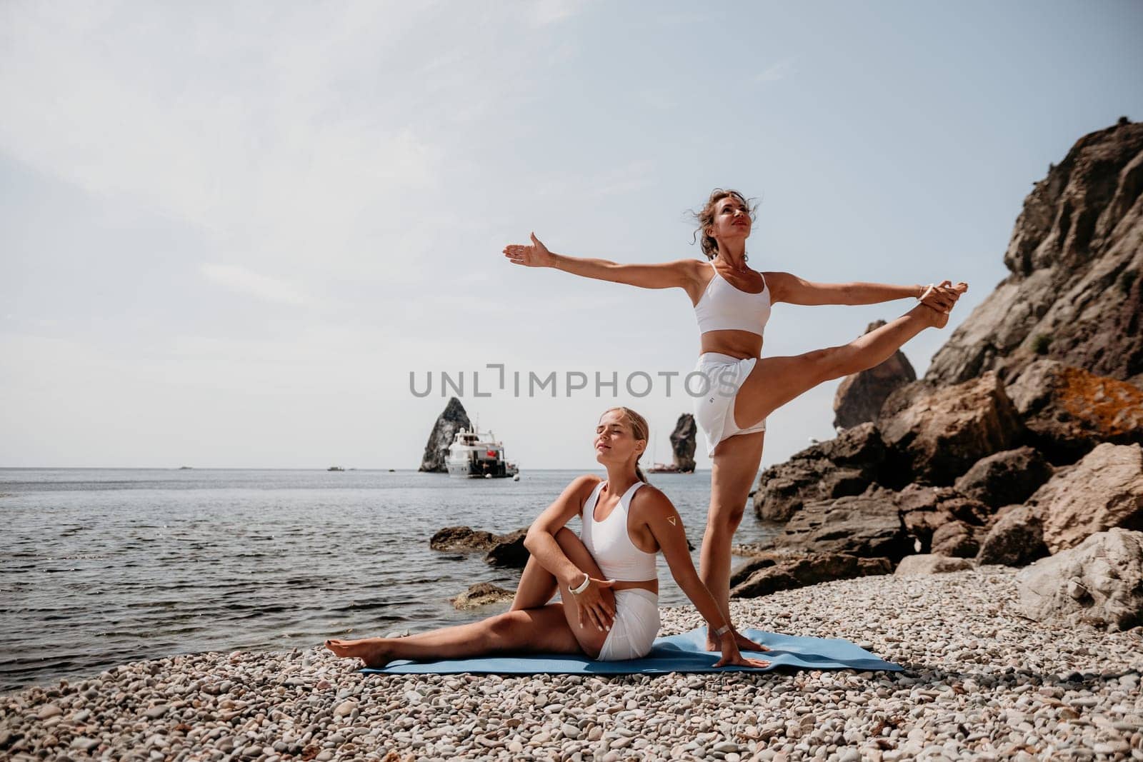 Woman sea yoga. Two Happy women meditating in yoga pose on the beach, ocean and rock mountains. Motivation and inspirational fit and exercising. Healthy lifestyle outdoors in nature, fitness concept. by panophotograph