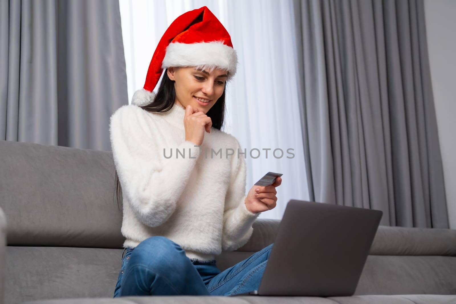 Smiling woman in Santa Claus hat holding a credit card and buying gifts online. by vladimka