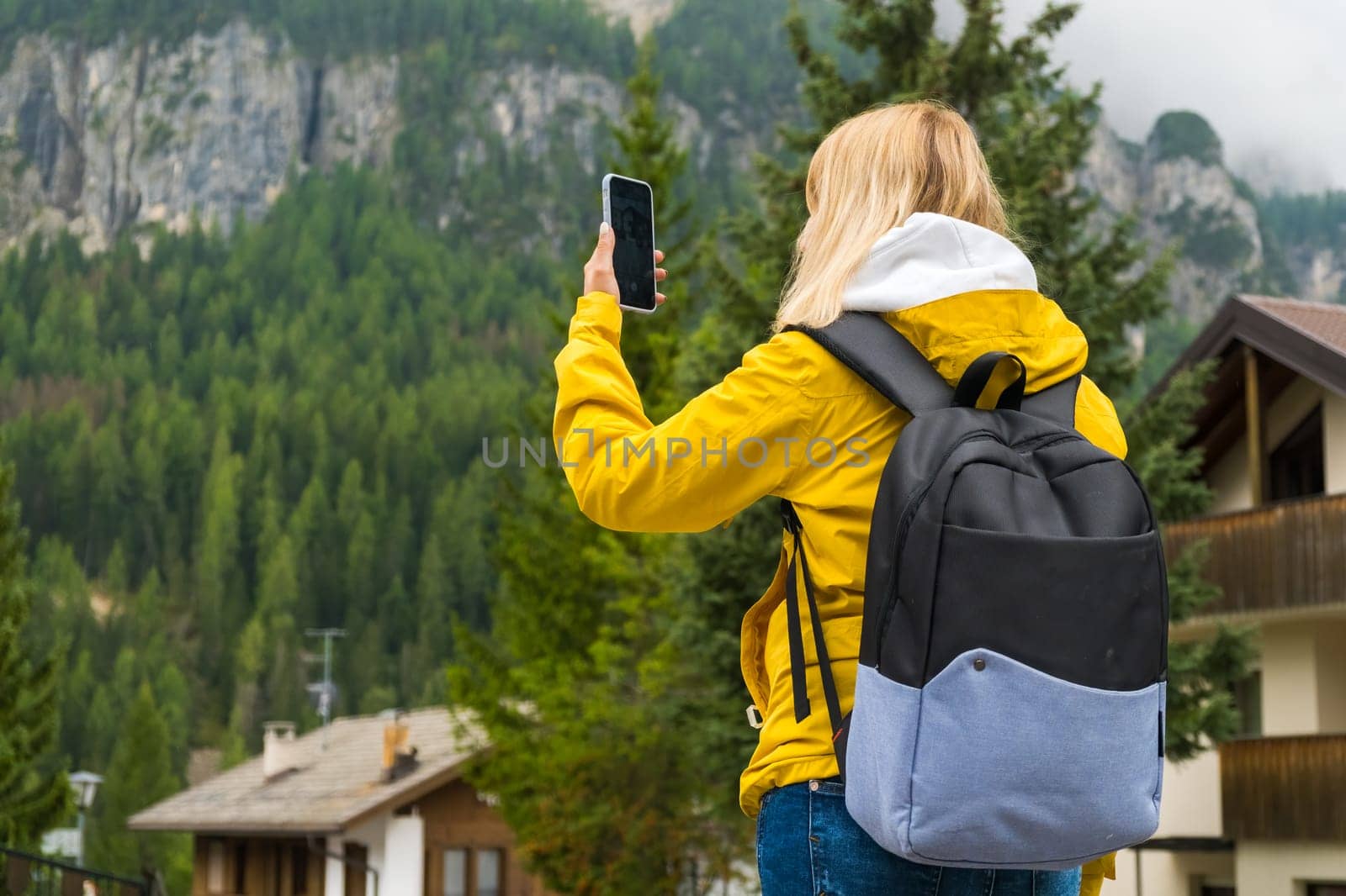 Blonde tourist captures moments on smartphone and enjoys vacation on Alpine mountains. Woman makes photos of mountain hills covered with clouds