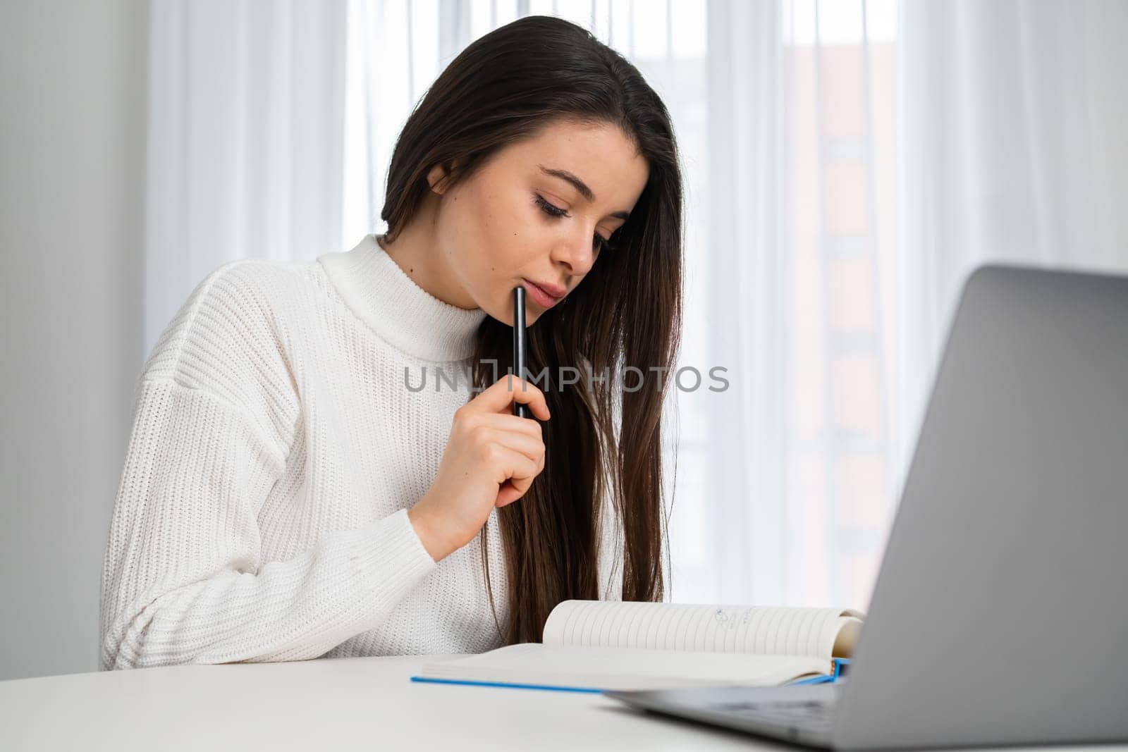 Smart student makes notes in the textbook during online lecture.