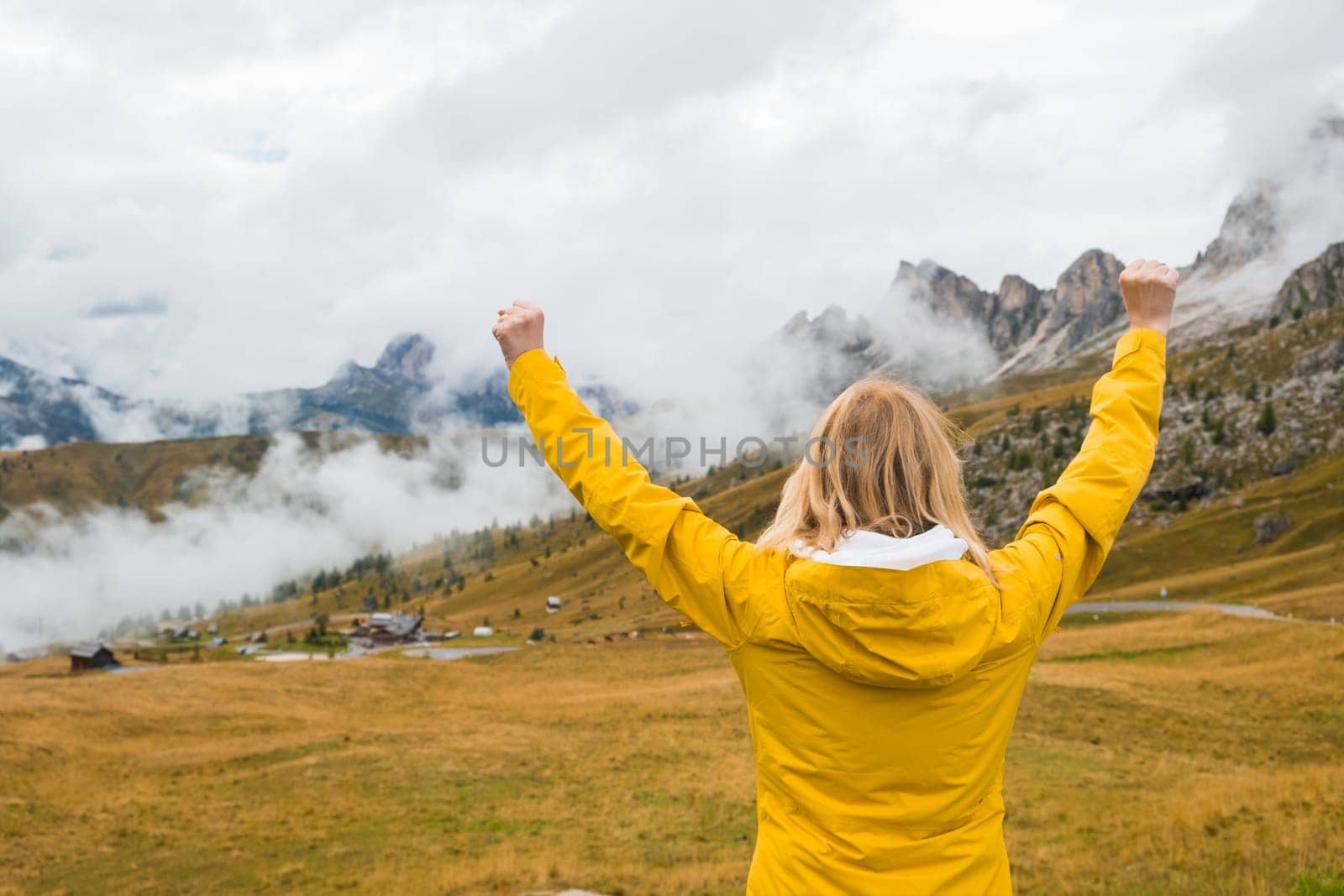 Happy female tourist spreads hands and enjoys in Italian Alps. Young woman feels happy to see Passo Giau pass in haze