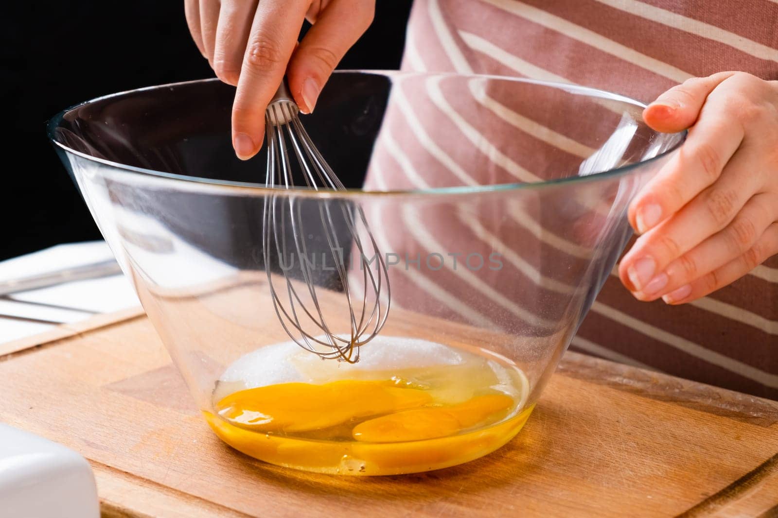 Close up of a womans hands whipping eggs for making dough on the wooden desk in the kitchen. Homemade cooking.