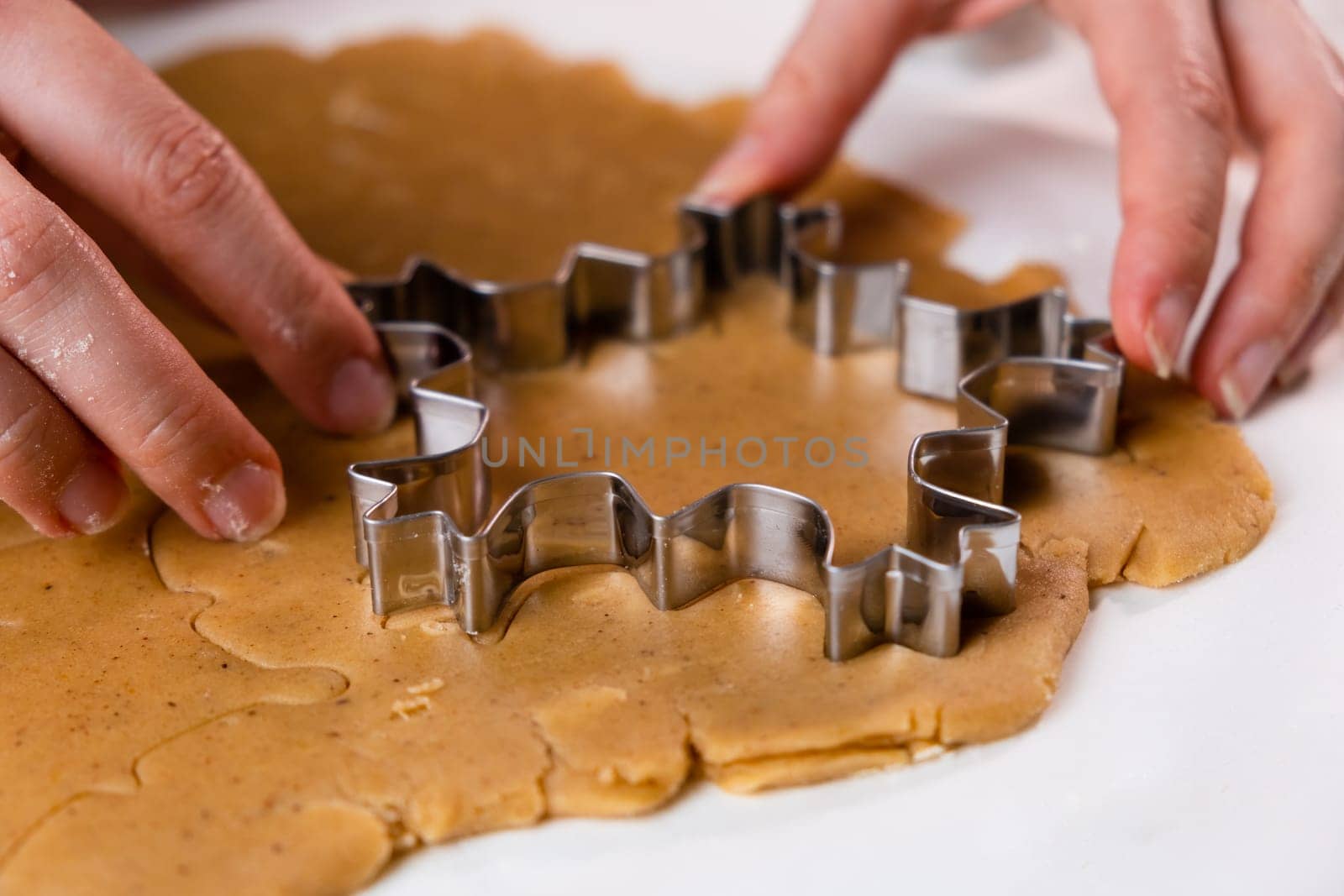 Close up woman hands cutting out cookies with metal mold from the shortcrust pastry. A metal forms in the form of snowflakes for making gingerbread for Christmas.