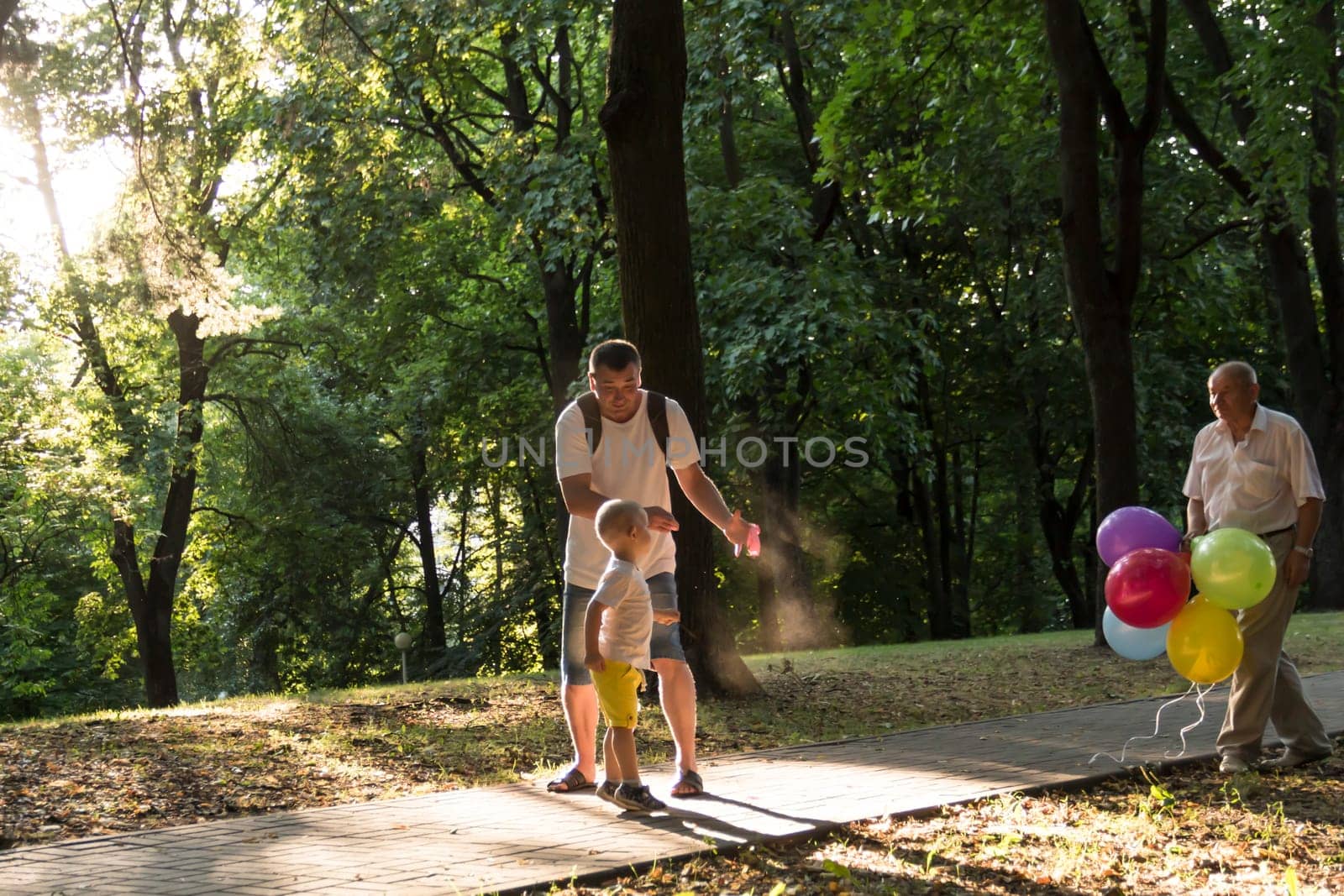 A little boy in yellow shorts bursts a balloon. The family is having fun in the park in the fresh air and celebrating the holiday. by Alla_Yurtayeva