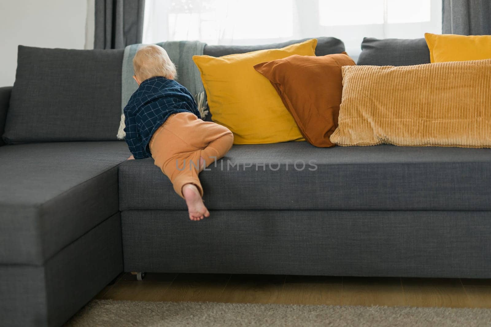 Toddler boy laughing having fun standing near sofa in living room at home. Adorable baby making first steps alone. Happy childhood and child care