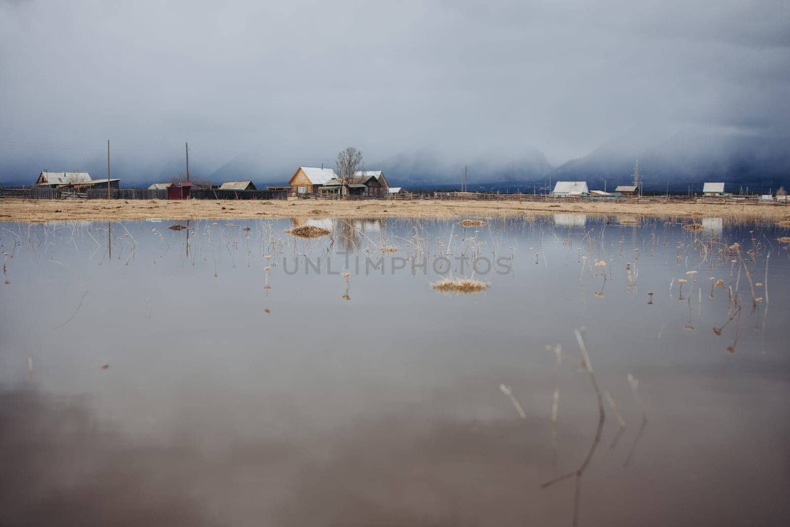 Mirror reflection from the water of melted snow in the village of Khurai-Khobok in the thick fog against the backdrop of the Sayan mountains