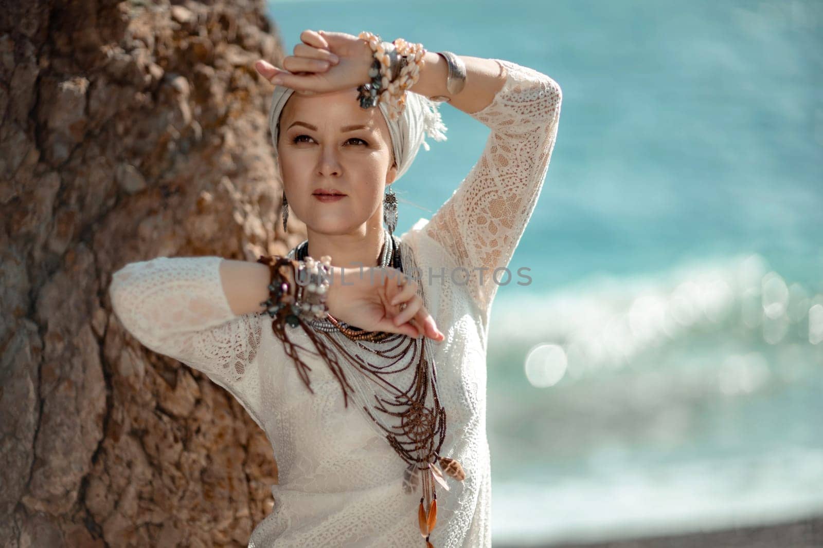 Middle aged woman looks good with blond hair, boho style in white long dress on the beach decorations on her neck and arms