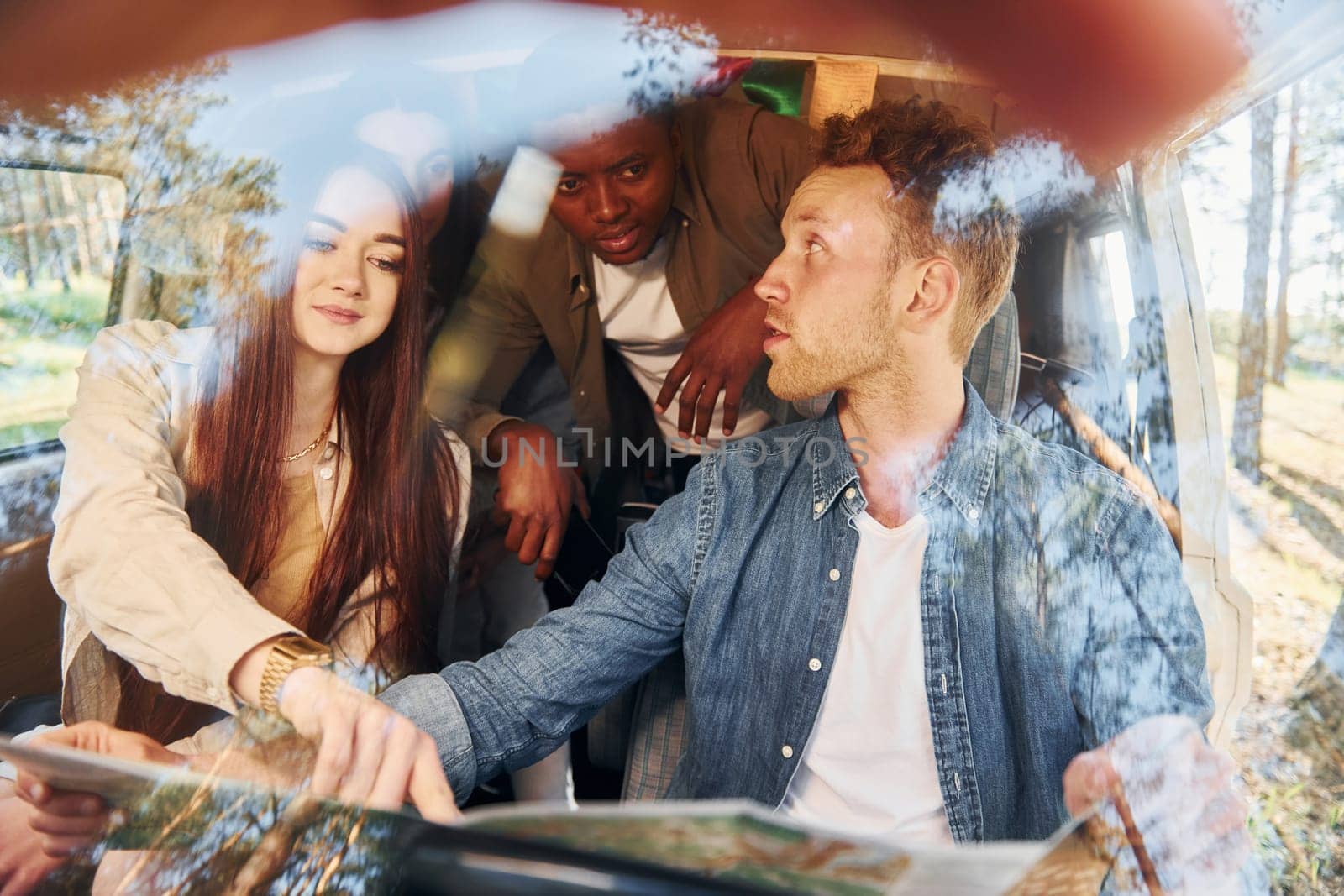 Sitting in the car. Group of young people is traveling together in the forest at daytime.