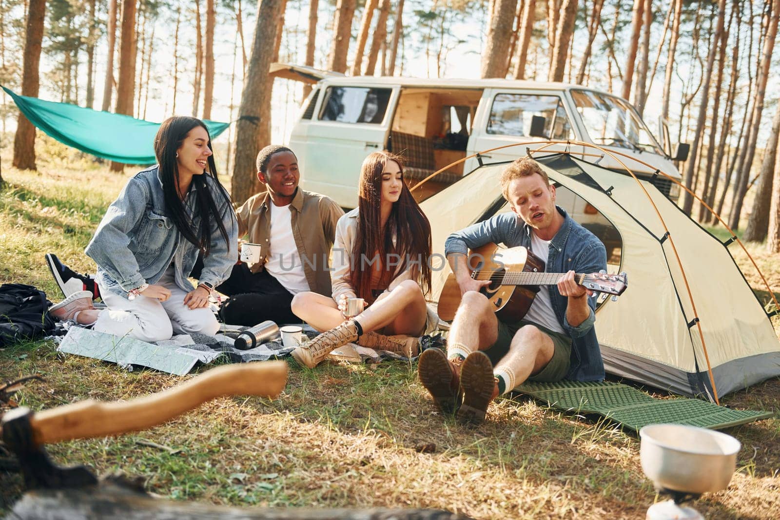 Man plays guitar. Group of young people is traveling together in the forest at daytime by Standret