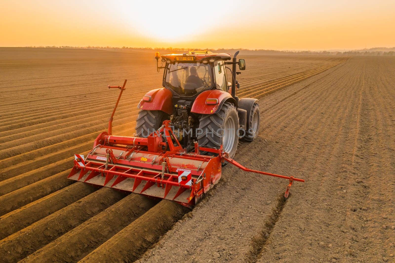 PRAGUE , CZECH REPUBLIC - MARCH 18 2022: Heavy tractor harrows in field dragging plow on purified soil. Contemporary agricultural transportation works at bright sunset in countryside